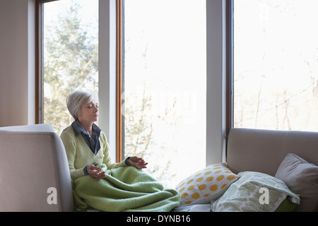 Ältere Frau, meditieren auf sofa Stockfoto