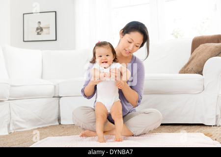 Mutter hilft Babymädchen im Wohnzimmer stehen Stockfoto