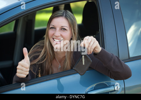 Eine lächelnde Frau ist aus dem Fenster gelehnt und zeigt einen Schlüssel Stockfoto