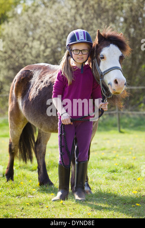 Ein junges Mädchen mit einem Pony draußen in der Natur an einem sonnigen Tag stehen und Lächeln in die Kamera Stockfoto