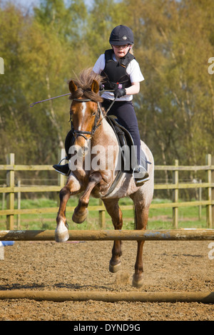 Ein Pony und Reiter Springen einen Zaun während einer Reitstunde Stockfoto