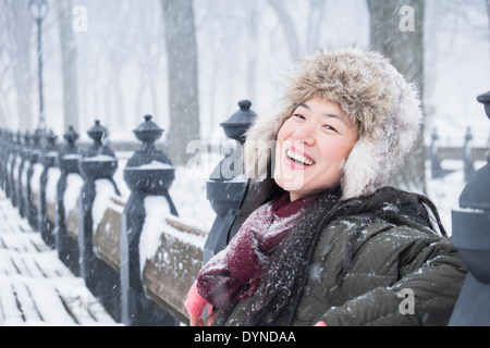Asiatische Frau sitzt auf der Parkbank im Schnee Stockfoto