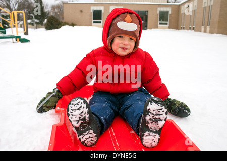 Gemischte Rassen Junge sitzt auf Schlitten im Schnee Stockfoto