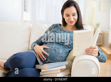 Schwangere Frau kaukasischen Baby Lesebücher auf sofa Stockfoto