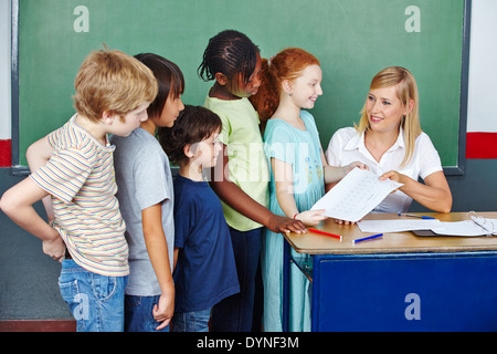 Lehrer benoten von Tests für Schüler in der Grundschule an ihrem Schreibtisch Stockfoto