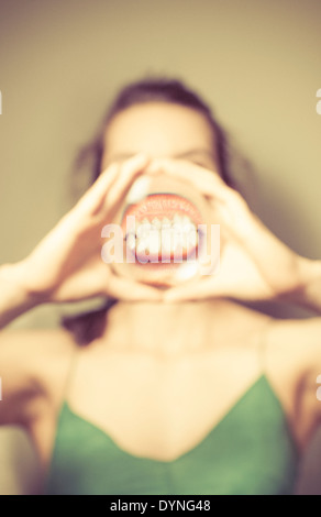 Junge Frau mit Lupe vor Mund, zeigt ihre Zähne. Stockfoto