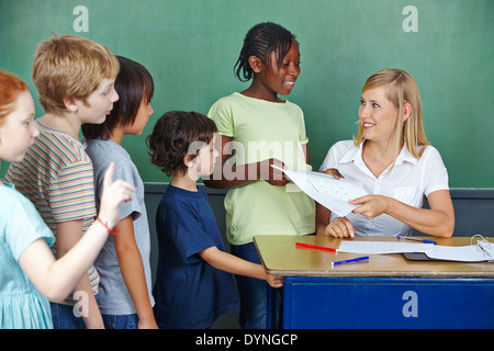 Grundschüler in Folge am Schalter des Lehrers zu ihren Tests zurück Stockfoto