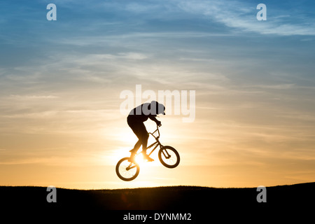 Junger Mann auf seinem BMX-Fahrrad in die Luft springen. Silhouette Stockfoto