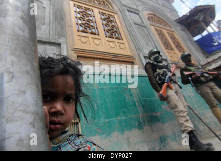 Srinagar, Kaschmir, Indien. Ein Kashmiri junges Mädchen steht auf der Straße als eine indische paramilitärische Soldaten Wache stehen während einer Kampagne Wahlveranstaltung am unten Stadtgebiet in Srinagar, der Sommerhauptstadt des indischen Teil Kaschmirs, 23.04.2014. Parlamentswahlen in Indien in neun Schritten zwischen 07 April und 12. Mai 2014 stattfinden werden, sagte des Landes Wahlkommission mit insgesamt 814,6 Millionen Menschen wahlberechtigt - rund 100 Millionen mehr als bei den Wahlen im Jahr 2009. Bildnachweis: Dpa picture Alliance/Alamy Live News Stockfoto