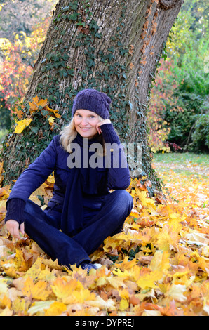 Frau mittleren Alters sitzen auf Herbstlaub und Blick in die Kamera Stockfoto