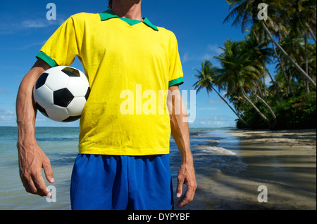 Brasilianischer Fußballspieler in Brasilien Teamfarben halten Fußball an abgelegenen Strand in Nordeste Bahia Stockfoto