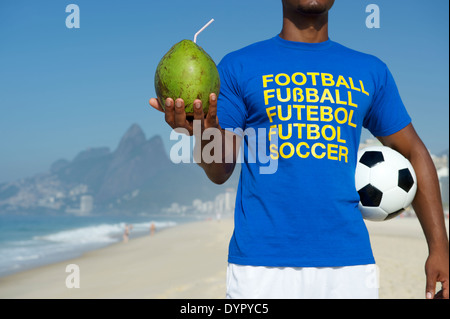 Brasilianische Fußballspieler in Multi Sprache Nachricht T-shirt Holding Fußball und trinken Kokosnuss Rio De Janeiro Stockfoto