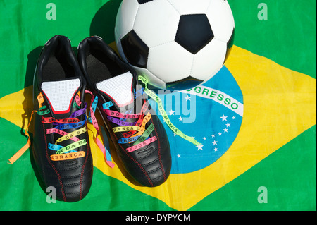 Viel Glück Fußballschuhe geschnürte mit brasilianischen Wunsch Bänder neben Ball auf brasilianische Flagge Fußball-Stollen Stockfoto