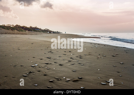 Rosa Himmel auf einen Sonnenuntergang am Strand mit einigen Kieselsteinen auf dem Sand. Stockfoto