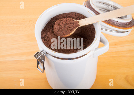Frische, gemahlener Kaffeebohnen in einem weißen Keramik Kanister auf einem Holztisch Stockfoto