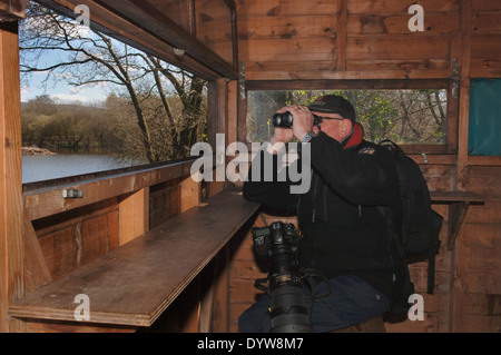 Ein Naturfotograf In seinen späten Seventies.Sitting In ein Vogel Hide.Using Fernglas. Stockfoto