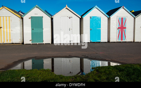 Eine Reihe von bunten Strandhäuschen spiegelt sich in einer Pfütze in Paignton, Devon England UK Stockfoto
