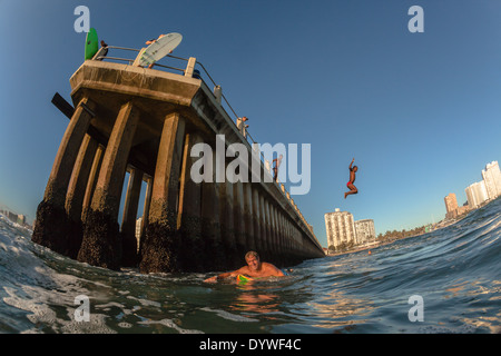 Surfer paddeln vorbei Pier andere Surfer Leute springen ins Meer Ozean Wasser Durban Südafrika Stockfoto