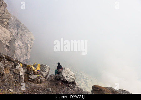 Sitzen Mann und Körben beladen mit Blöcken von Schwefel, Kawah Ijen, Banyuwangi Regency, Ost-Java, Indonesien Stockfoto