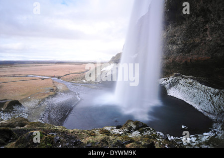 Fuß hinter die wispy Wasserfall Seljalandsfoss im Süden Islands, an einem trüben Tag. Stockfoto