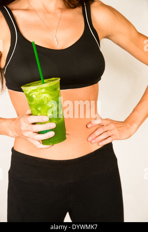 Frau hält grüne Frucht Smoothie Taille Ebene zeigt gesunden schlanken Körper Stockfoto