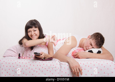 Junges Mädchen und ein Mann im Bett. Schönes Mädchen hat gepflegte Nägel auf der Hand, der Kerl gerade Fußball im Fernsehen Stockfoto