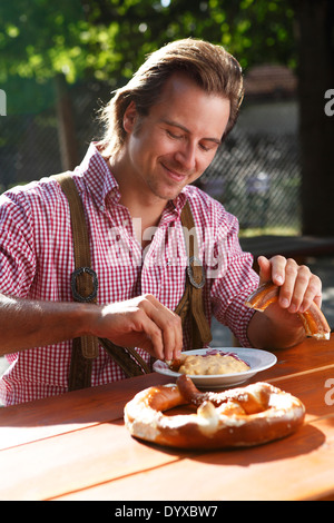 Attraktiver Mann isst traditionelle Käse mit Brezel in einem bayerischen Biergarten Stockfoto