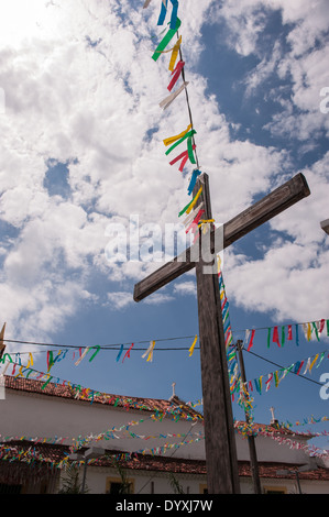 Itaparica Island, Bundesstaat Bahia, Brasilien. Itaparica-Stadt. Holzkreuz mit bunten Girlanden außerhalb einer kolonialen Kirche. Blauer Himmel und weiße Wolken. Stockfoto