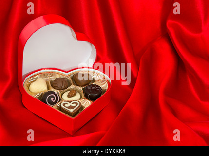 Pralinen in goldenes Herz-Form-Box über rote Seide Hintergrund. Valentinstag Geschenk. Platz für Ihren text Stockfoto
