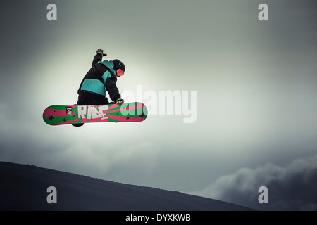 Snowboarder mit Helm und Brille führt einen Greifer Antenne Sprung und zeigt ein buntes Design auf der Unterseite der Platine. Stockfoto