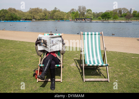 Frau liest eine Zeitung sitzt auf einem Liegestuhl im Hyde Park in London Vereinigtes Königreich Stockfoto
