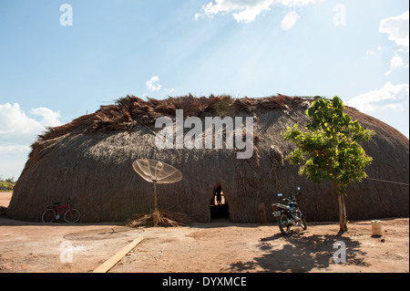 Xingu indigenen Park, Mato Grosso, Brasilien. Aldeia Matipu. Traditionelle Oca Einfamilienhaus, Fahrrad, Satelliten-Schüssel, Motorrad und Baum. Kombination von traditioneller Kultur und neuen Technologien. Stockfoto