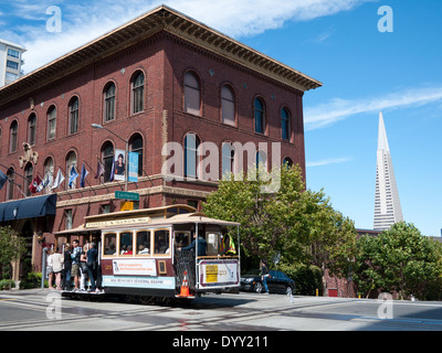 Powell-Mason Cable Car übergibt die University Club of San Francisco, mit der Transamerica Pyramide im Hintergrund. Stockfoto