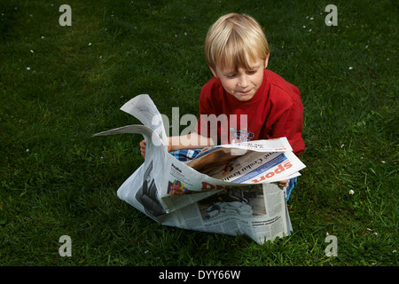 Ein Kind blonde junge liest Zeitung außerhalb am grünen Rasen Stockfoto