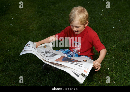 Ein Kind blonde junge liest Zeitung außerhalb am grünen Rasen Stockfoto