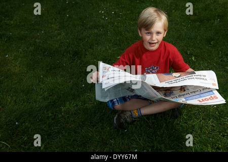 Ein Kind blonde junge liest Zeitung außerhalb am grünen Rasen Stockfoto