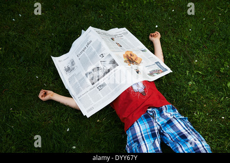 Ein Kind blonde junge liest Zeitung außerhalb am grünen Rasen Stockfoto