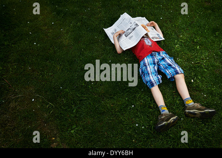 Ein Kind blonde junge liest Zeitung außerhalb am grünen Rasen Stockfoto