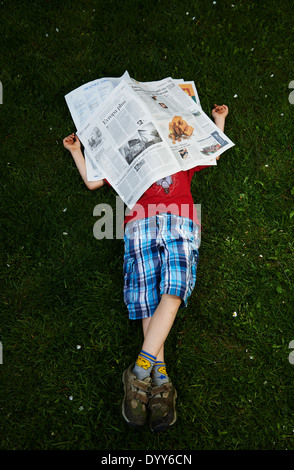 Ein Kind blonde junge liest Zeitung außerhalb am grünen Rasen Stockfoto