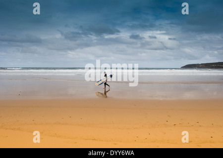 einsamer Surfer zu Fuß an den sehr niedrigen Gezeiten am goldenen Sandstrand mit langes Brett. große Foto. dramatische Gewitterhimmel. Australien Stockfoto