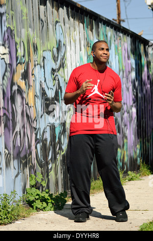 Ein junger Mann, African American, gerne Musik hören über Kopfhörer, tanzen vor Graffitiwand. Stockfoto