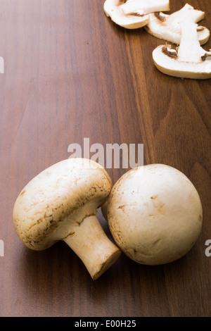 Zwei Taste Pilze/Champignons auf braunem Hintergrund mit drei Scheiben des Pilzes in der rechten oberen Ecke. Stockfoto