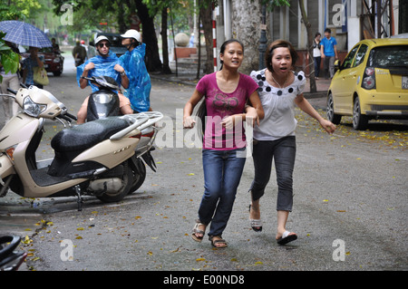 Zwei vietnamesische Mädchen laufen im Regen in Hanoi, Vietnam Stockfoto