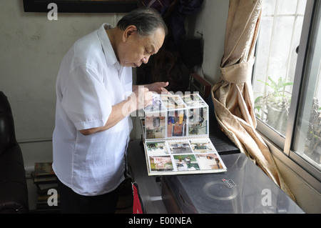 Ein älterer vietnamesischer Mann schaut sich ein Familienfoto-Album am Fenster in seiner Wohnung in Hanoi, Vietnam an Stockfoto