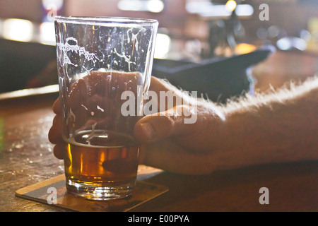 Nahaufnahme eines Menschen Hand greifen meist betrunken, Glas Bier mit Wanderwegen von seifenlösungen auf einer bar Coaster Stockfoto