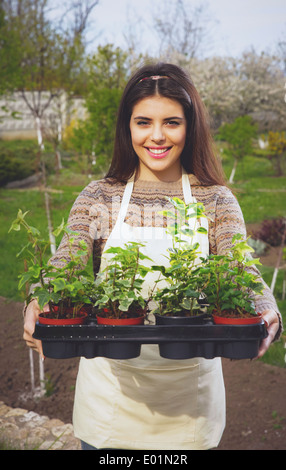 Lächelnde süße Frau mit Blumen in Töpfen im Garten Stockfoto