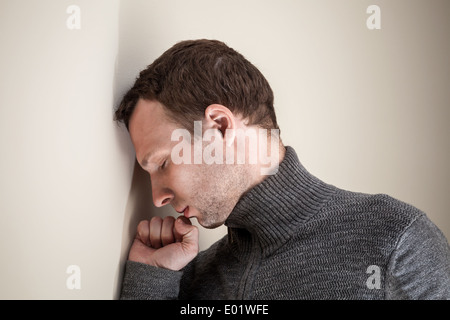 Traurig kaukasischen Jüngling legte seinen Kopf und seine Faust auf weiße Wand Stockfoto