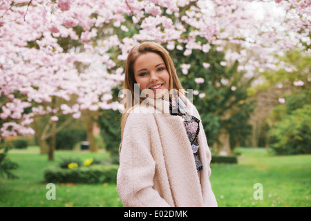 Glückliche junge Frau posiert im Frühjahr blühen Garten. Ziemlich kaukasischen weibliches Modell stehen im Freien in einem Park. Stockfoto