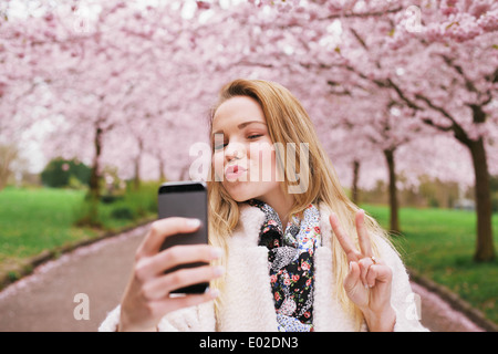 Attraktive junge Frau posiert für Selfie. Schöne Frau im Frühjahr blühen Park unter Selbstbildnis mit Handy. Stockfoto