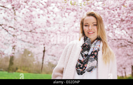 Attraktive junge Frau, Blick in die Kamera Lächeln im Frühlingspark im Freien stehen. Schöne junge Dame warmen Mantel tragen. Stockfoto